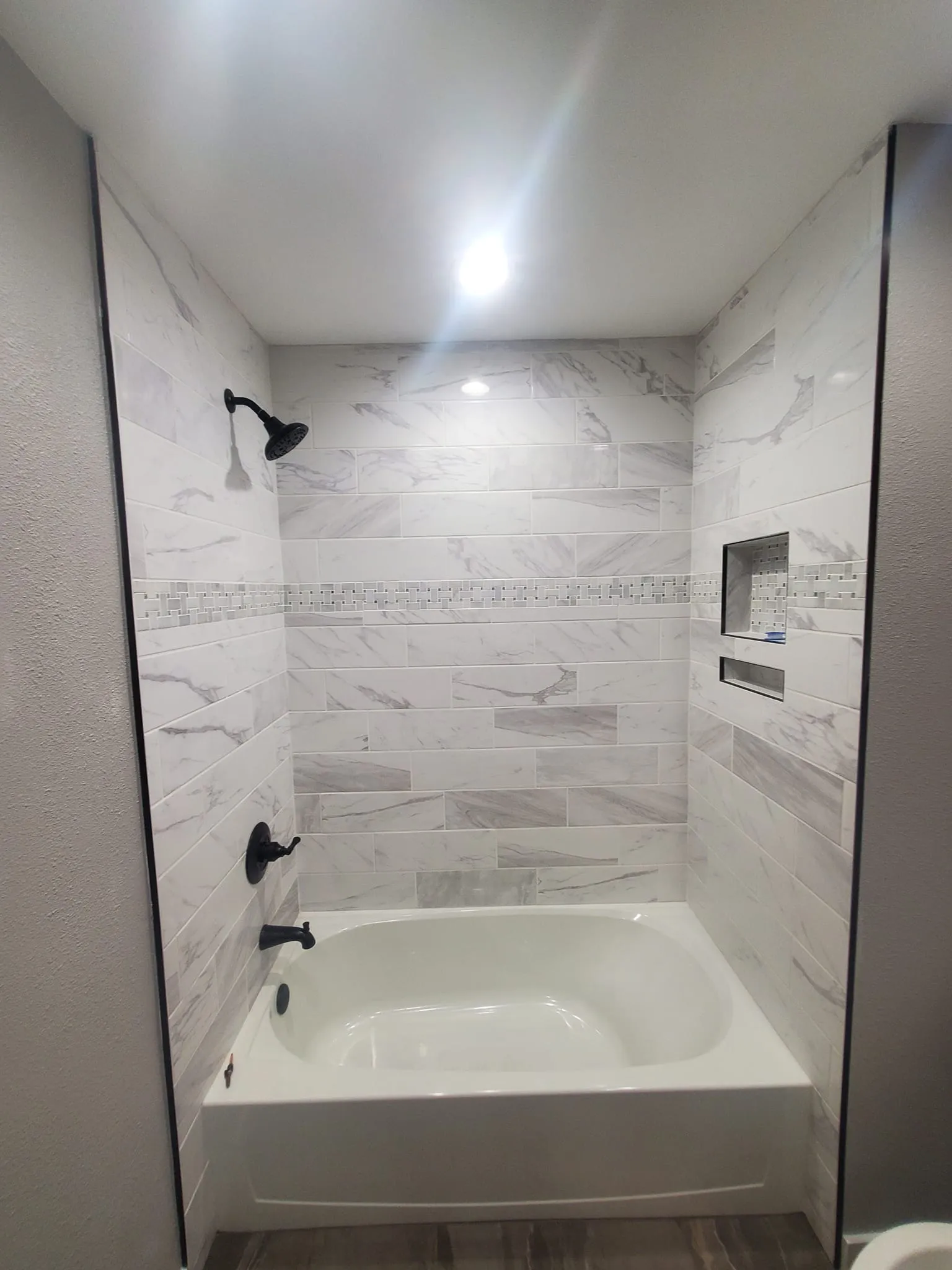Finished bathroom with subway-pattern marble tile shower and bronze fixtures.